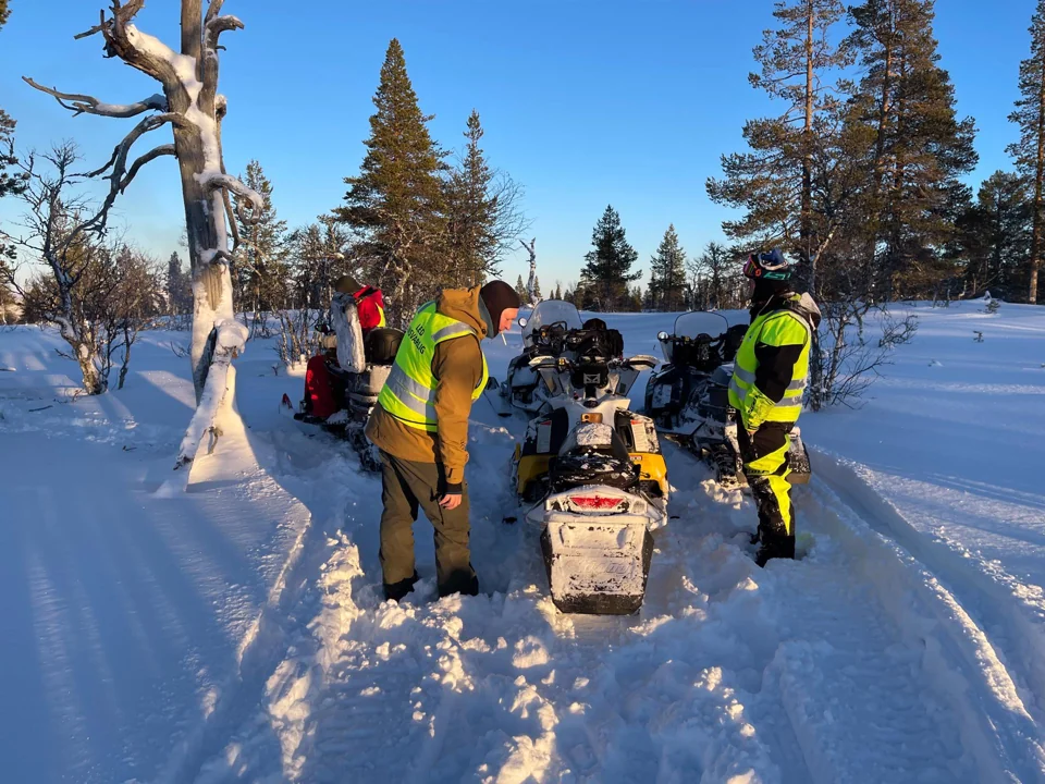Folk i synlighetsvester samlet ved snøscootere i vinterløypa