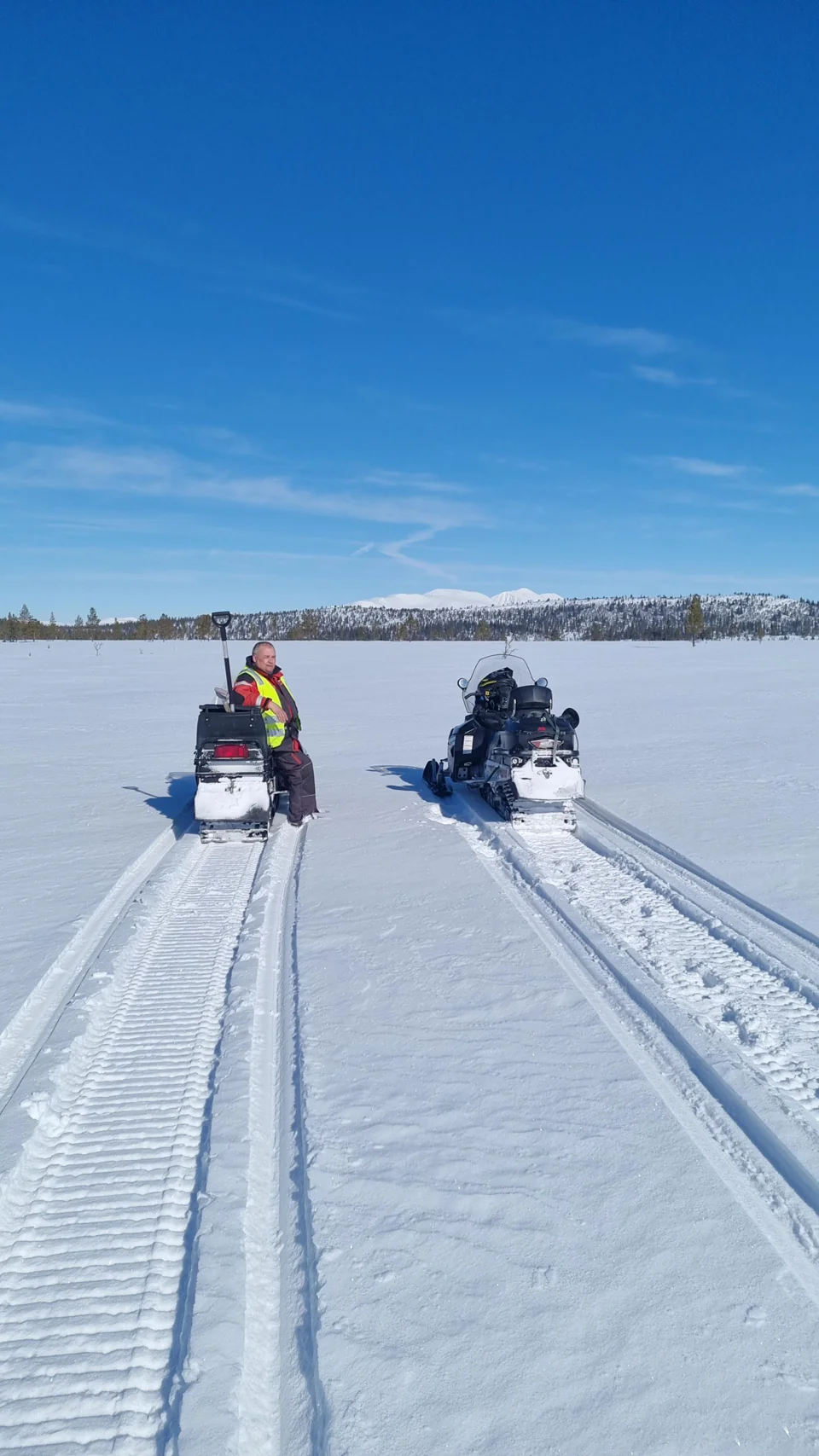 To snøscootere i et åpent vinterlandskap med fjell i bakgrunnen